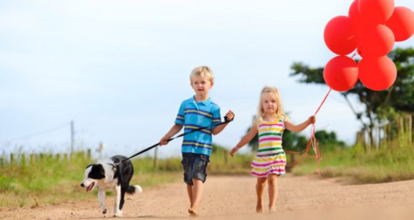 Mädchen, Junge und Hund im Sommer auf Sandweg, das Mädchen mit roten Luftballons in der Hand