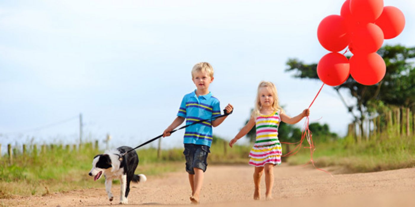 Mädchen, Junge und Hund im Sommer auf Sandweg, das Mädchen mit roten Luftballons in der Hand