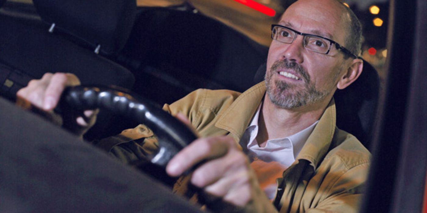 Mann mit Bart und Brille hinter dem Steuer eines Autos bei Nacht