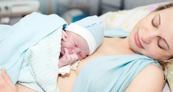 Mutter liegt im Krankenhausbett mit einem Neugeborenem auf der Brust.