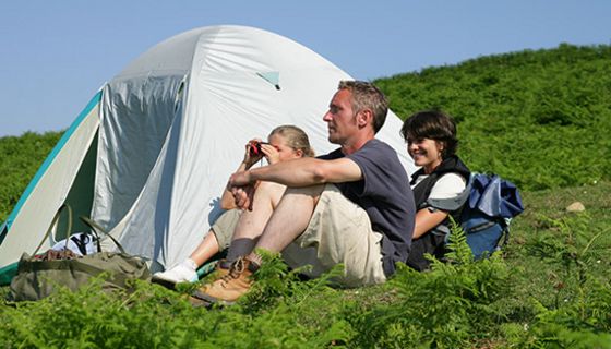 Vater, Mutter, Kind (Mädchen, ca. 10 )mit Fernglas, sitzen vor Igluzelt am Berghang zwischen Farnkraut