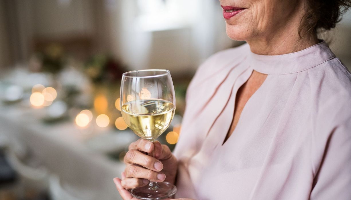 Ältere Frau hält ein Glas Weißwein in der Hand.