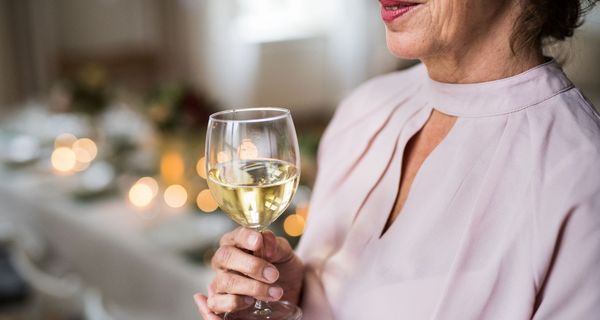 Ältere Frau hält ein Glas Weißwein in der Hand.