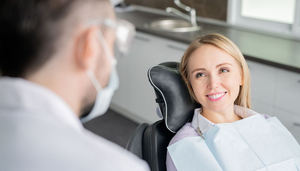 Junge Frau, sitzt auf einem Zahnarztstuhl und lächelt.