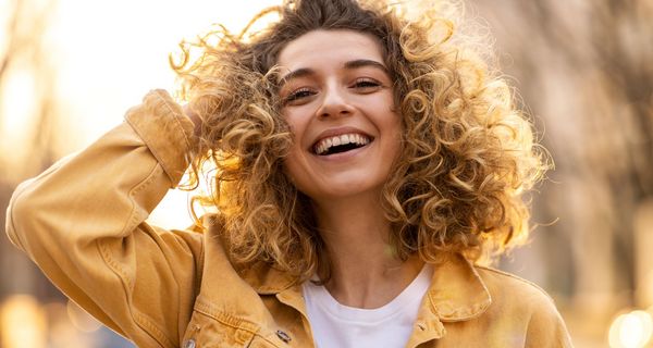 Junge Frau mit Locken, lacht in die Kamera.