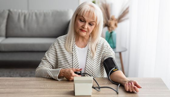 Ältere Frau, misst zu Hause ihren Blutdruck mit einem Oberarm-Messgerät.
