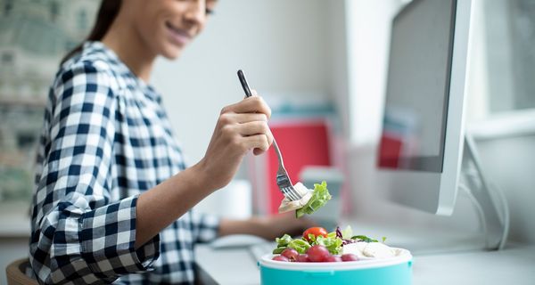 Frau, isst an ihrem Schreibtisch einen Salat.