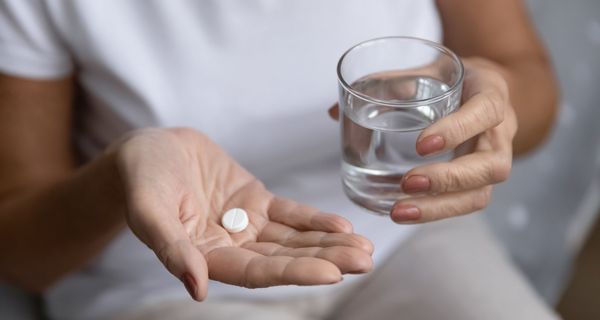 Frau, hält ein Glas Wasser und Tabletten in der Hand.