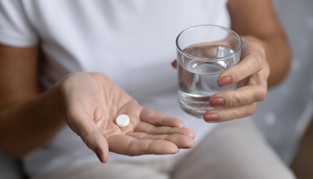 Frau, hält ein Glas Wasser und Tabletten in der Hand.