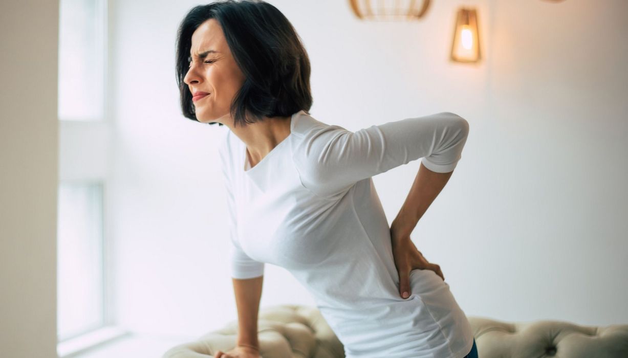 Frau hält sich den Rücken, ihr Gesicht ist schmerzverzerrt.