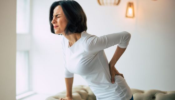 Frau hält sich den Rücken, ihr Gesicht ist schmerzverzerrt.