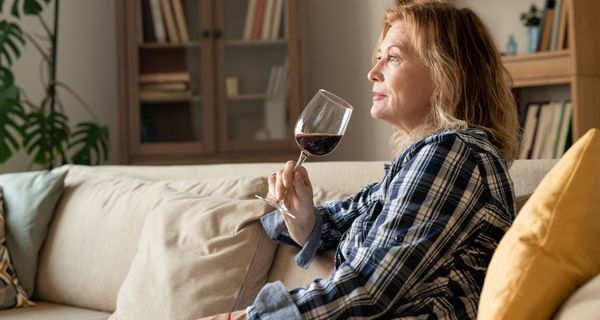 Eine mittelalte Frau sitzt auf dem Sofa und trinkt allein ein Glas Wein.