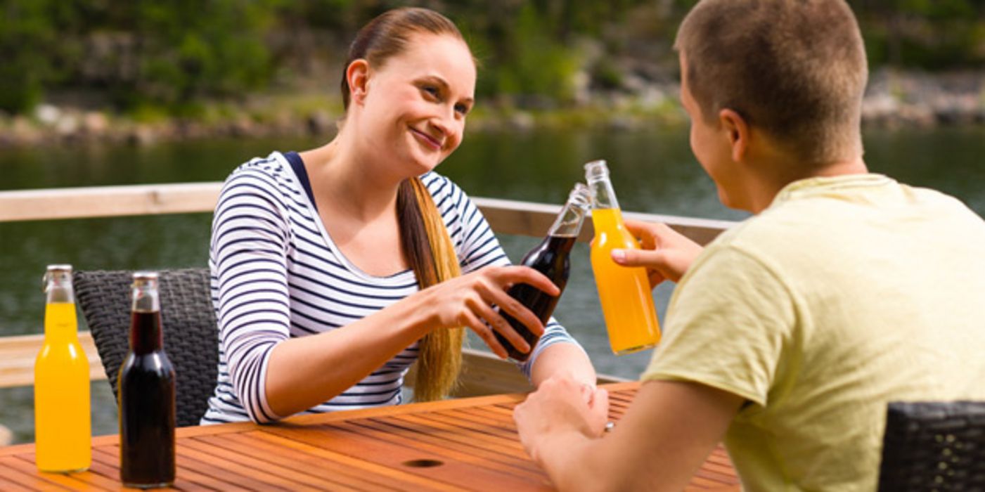 Junges Paar auf Seeterrasse prostet sich mit Limoflaschen zu