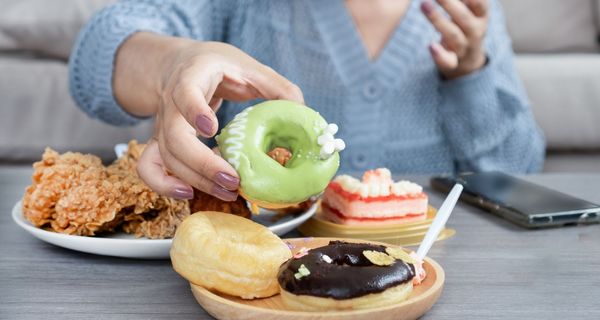 Frau vor mehreren Tellern mit Donuts, Fast Food und Kuchen.