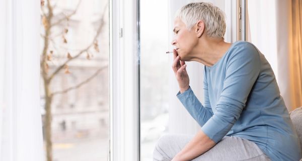 Ältere Frau, sitzt auf einer Fensterbank und raucht.