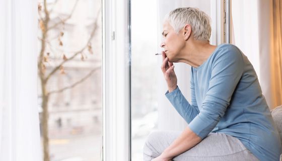 Ältere Frau, sitzt auf einer Fensterbank und raucht.