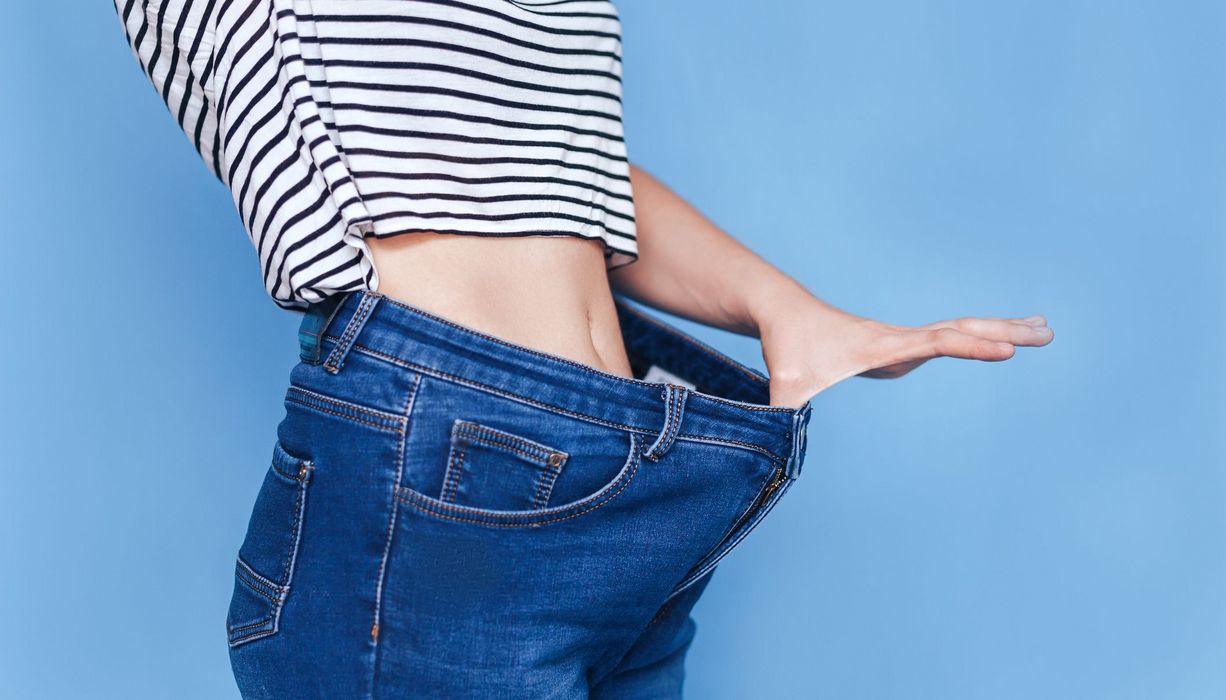 Frau, zeigt anhand dem Bund ihrer Jeans, wie viel sie abgenommen hat.