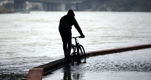 Mann, schiebt sein Fahrrad durch überflutete Straßen.