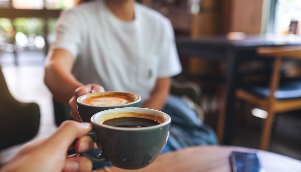 Zwei Männer, prosten sich mit einer Tasse Kaffee zu.