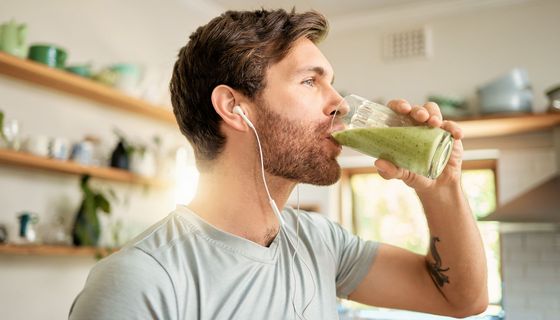 Junger Mann mit Kopfhörern trinkt einen grünen Soothie.