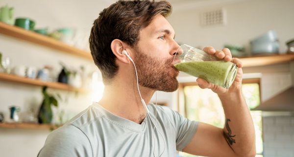 Junger Mann mit Kopfhörern trinkt einen grünen Soothie.
