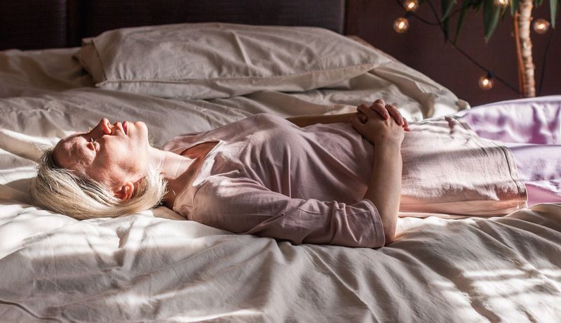 Frau im Alter zwischen 40 und 60 Jahren liegt auf dem Rücken im Schlafanzug auf dem Bett. Sie blickt an die Decke.