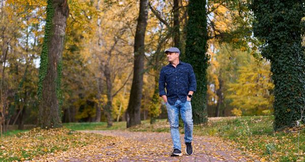 Ein Mann mit einer Schiebermütze geht im frühen Herbst durch einen Park.