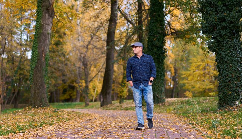 Ein Mann mit einer Schiebermütze geht im frühen Herbst durch einen Park.