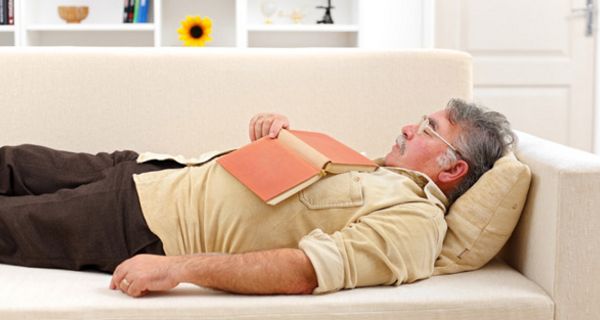 Mann schläft auf einer Couch mit Buch auf dem Bauch
