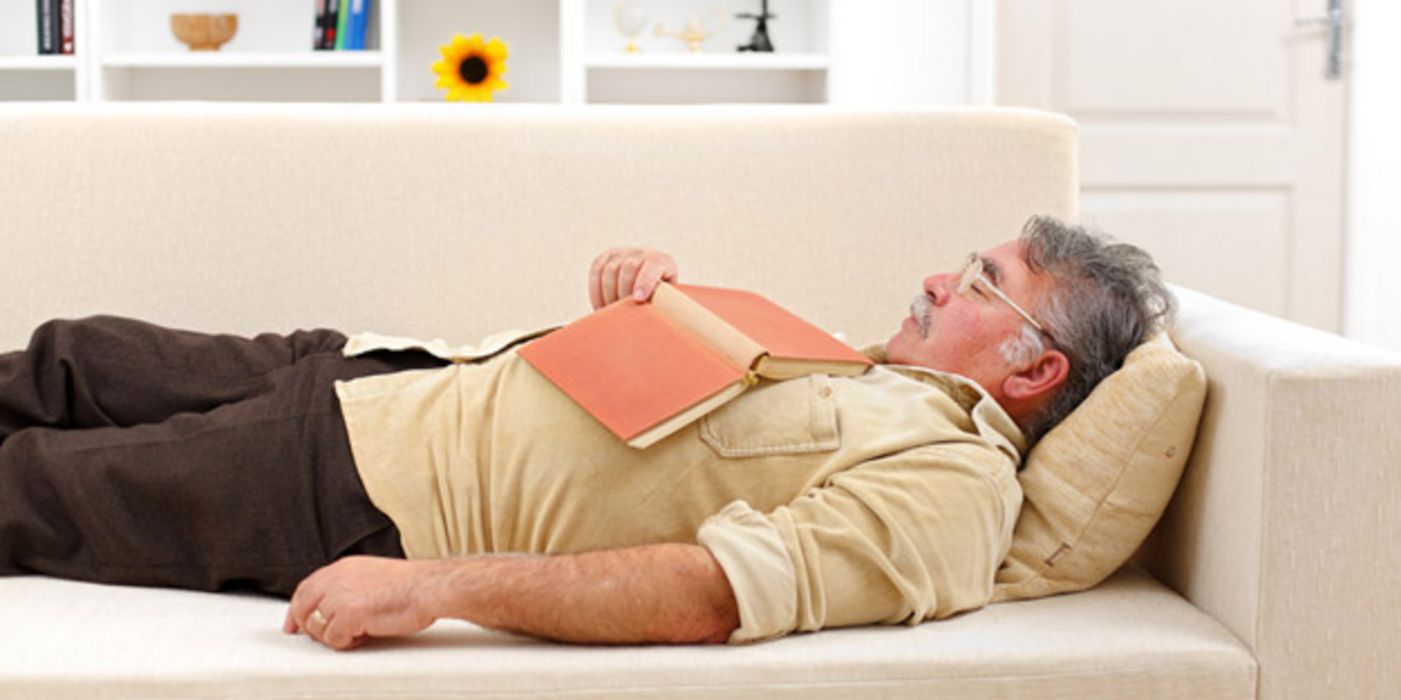 Mann schläft auf einer Couch mit Buch auf dem Bauch