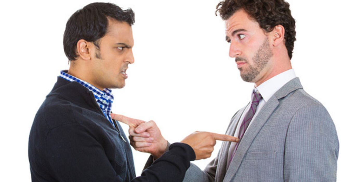 Zwei Männer in den 30ern in lässiger Bürokleidung stehen sich wütend gegenüber und deuten beschuldigend mit dem Zeigefinger aufeinander