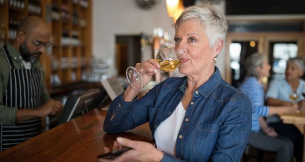 Ältere Frau, trinkt ein Glas Wein.