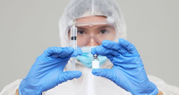 Forscher hält Impfstoff und Nadel in beiden Händen.