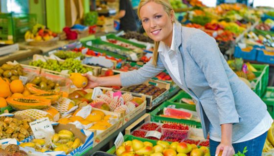 Frau an einem Marktstand mit Obst und Gemüse