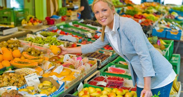 Frau an einem Marktstand mit Obst und Gemüse