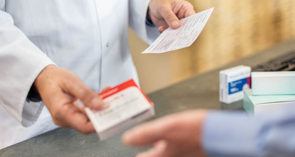 Patient tauscht ein rosa Rezept in der Apotheke gegen ein Medikament aus.