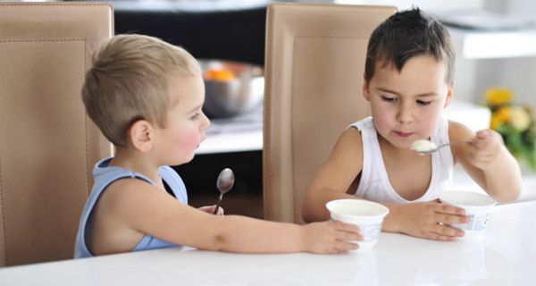 Zwei kleine Jungen essen Joghurt, der eine bietet dem anderen seinen Becher an