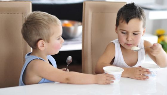 Zwei kleine Jungen essen Joghurt, der eine bietet dem anderen seinen Becher an