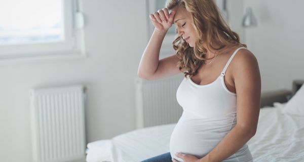 Junge schwangere Frau, fasst sich an den Kopf.