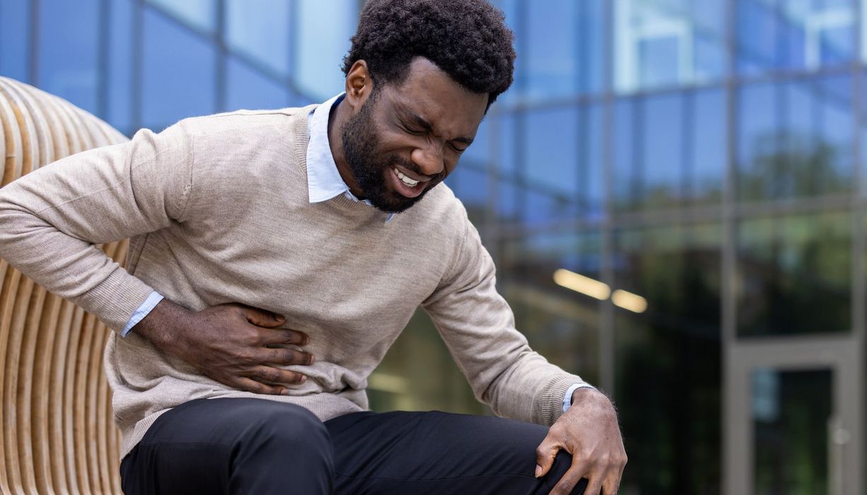 Junger Mann sitzt auf einer Bank und hält sich den Oberbauch, etwa auf Höhe des Magens.