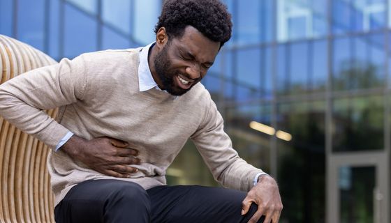 Junger Mann sitzt auf einer Bank und hält sich den Oberbauch, etwa auf Höhe des Magens.