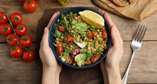 Hände umfassen eine Schüssel mit leckerem Linsensalat.