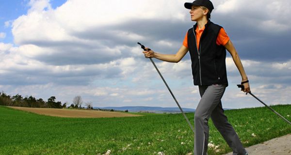 Frau mittleren Alters in Sportkleidung beim Nordic-Walking auf einem Weg durch blühende Wiesen