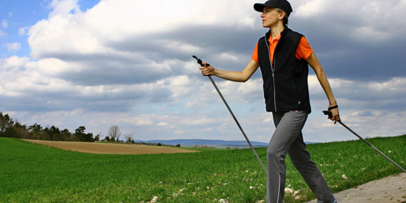 Frau mittleren Alters in Sportkleidung beim Nordic-Walking auf einem Weg durch blühende Wiesen