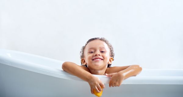 Kind, sitzt in der Badewanne, schaut heraus und lacht.