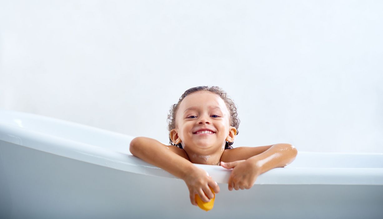Kind, sitzt in der Badewanne, schaut heraus und lacht.