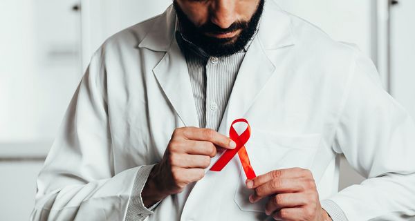 Ein Mann mit Bart steckt sich eine rote AIDS-Schleife an den Kittel.