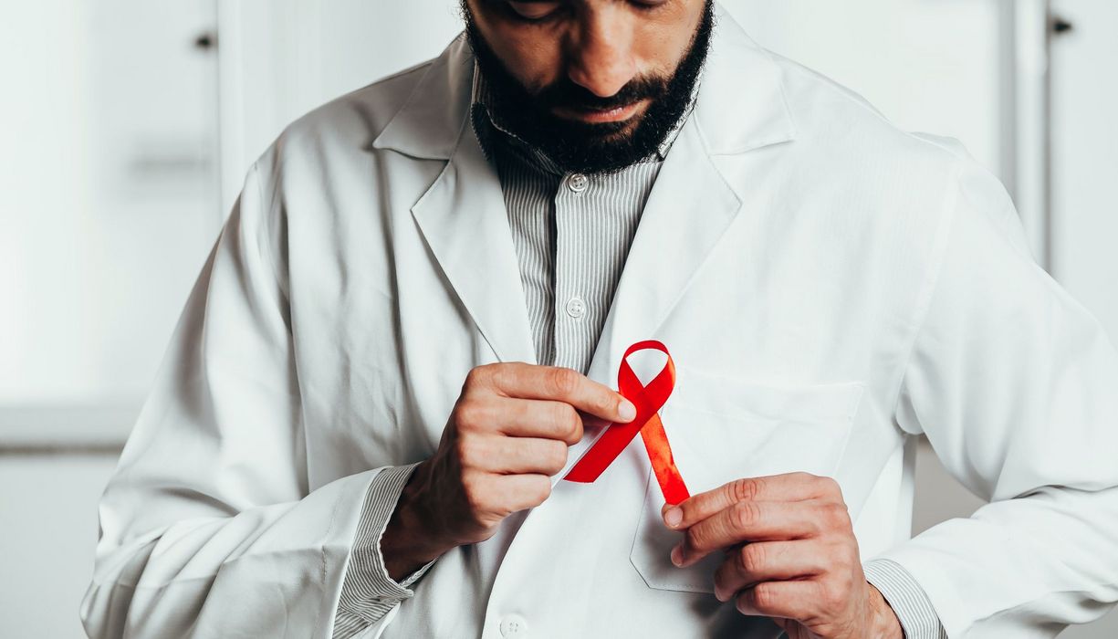 Ein Mann mit Bart steckt sich eine rote AIDS-Schleife an den Kittel.