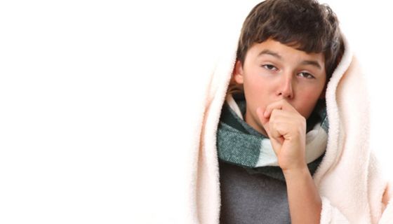 Hustender Junge mit Schal um den Hals und Decke über dem Kopf