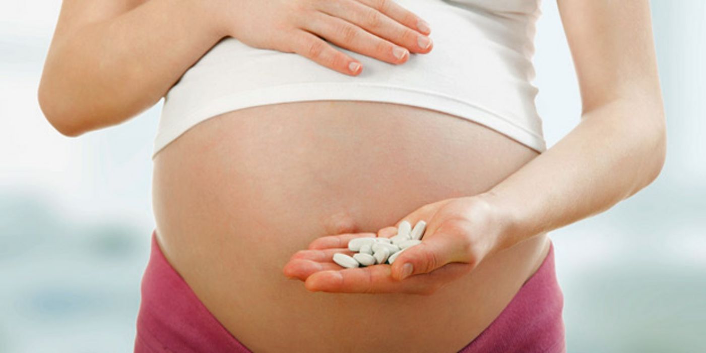Schwangere fasst sich mit der einen Hand an den Bauch, in der anderen hält sie einige Tabletten